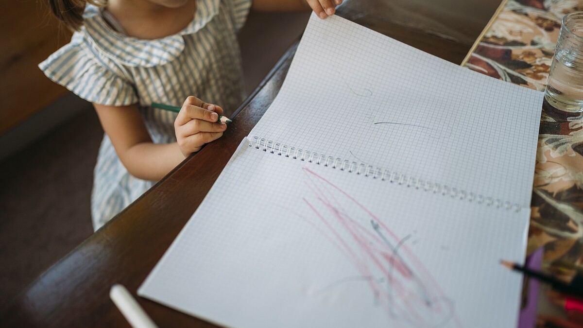 Enfant réalisant un dessin simple avec des crayons de couleur sur une table